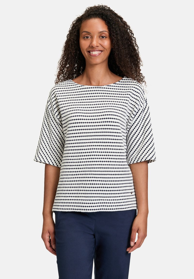 Haut rayé blanc et marine à manches courtes, avec un col rond et un motif texturé en points sur le tissu.