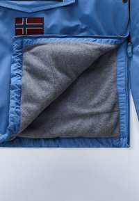 Blue jacket with a soft gray fleece lining and a pocket featuring a red and blue flag patch. Smooth exterior with zip closure.