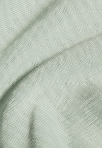 Light green knit fabric featuring a soft texture and a fine, even weave, with gently undulating folds creating a dynamic visual effect.