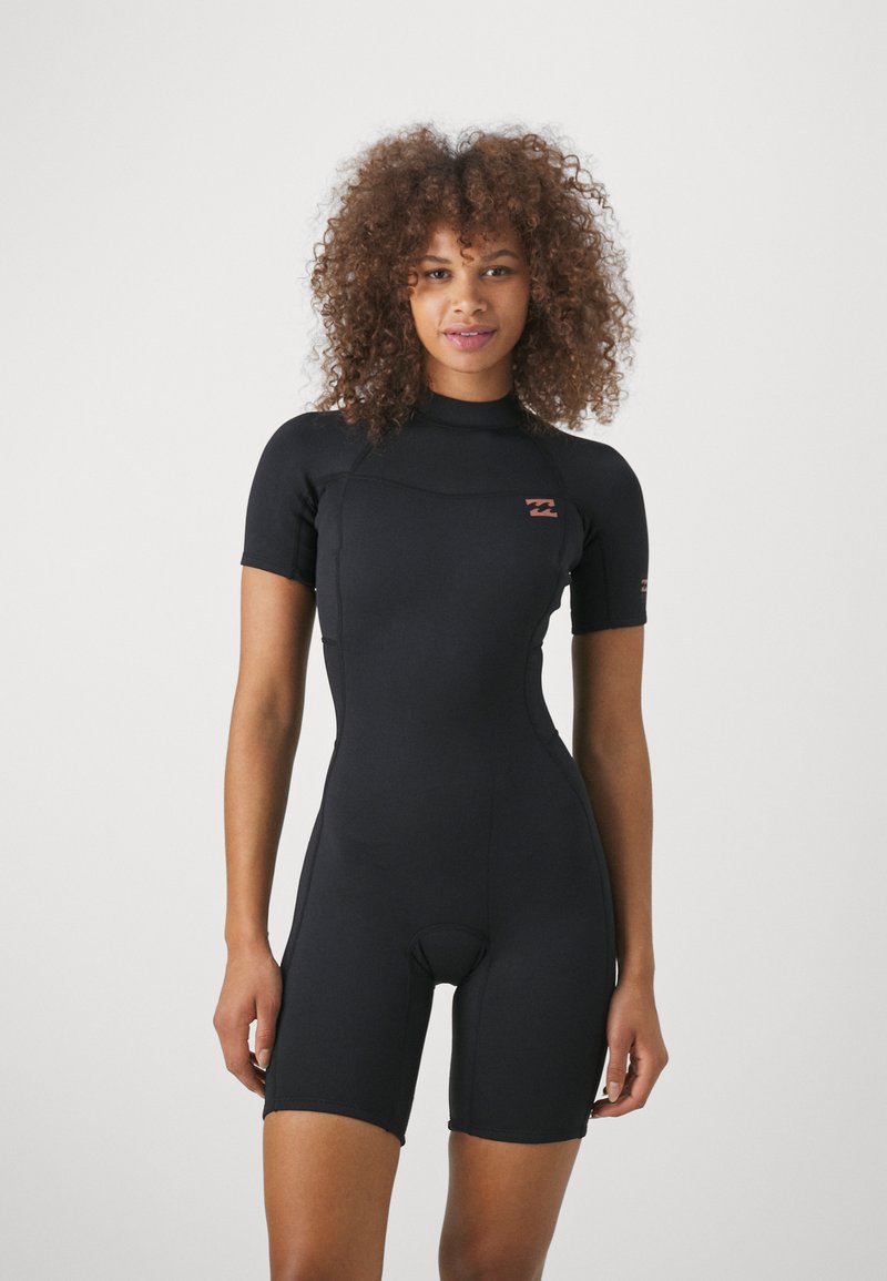 Combinaison de plongée noire à manches courtes avec un design ajusté, fabriquée en matériau extensible. Elle dispose d'un col montant et d'un petit logo sur la poitrine.