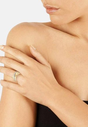 Nahaufnahme der Schulter und Hand einer Person mit einem goldenen und silbernen Ring am Ringfinger, sichtbare Lippen und ein Teil des Halses, helle Hautfarbe.