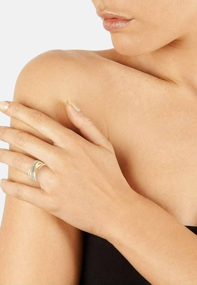 Close-up of a person’s shoulder and hand with a gold and silver ring on the ring finger, lips and part of neck visible, light skin tone.