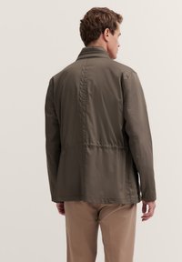 Olivegrüne, leichte Jacke mit Kragen, elastischem Bund und glattem Stoff. Verfügt über ein schlichtes, modernes Design ohne sichtbare Hardware.