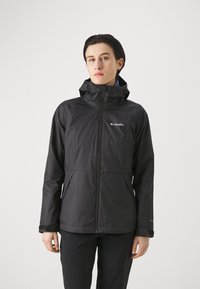 Black waterproof jacket featuring a high collar, zippered front, two side pockets, and a hood. Columbia logo visible on the chest.