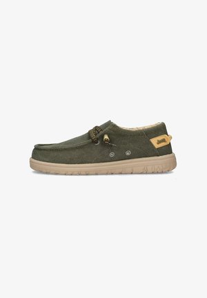 Scarpa slip-on verde in tela con suola in gomma beige, caratterizzata da lacci decorativi, due fori per lacci e un'etichetta con logo sul tallone.