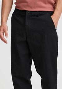 Pantalones de algodón negros con corte recto, con cierre de botones, bolsillos laterales y textura suave.
