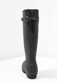 Schwarze Gummistiefel bis zum Knie mit strukturiertem Finish, einem rückseitigen Schnallenriemen und vertikalen Linien, die für zusätzliche Details entlang des Schafts verlaufen.