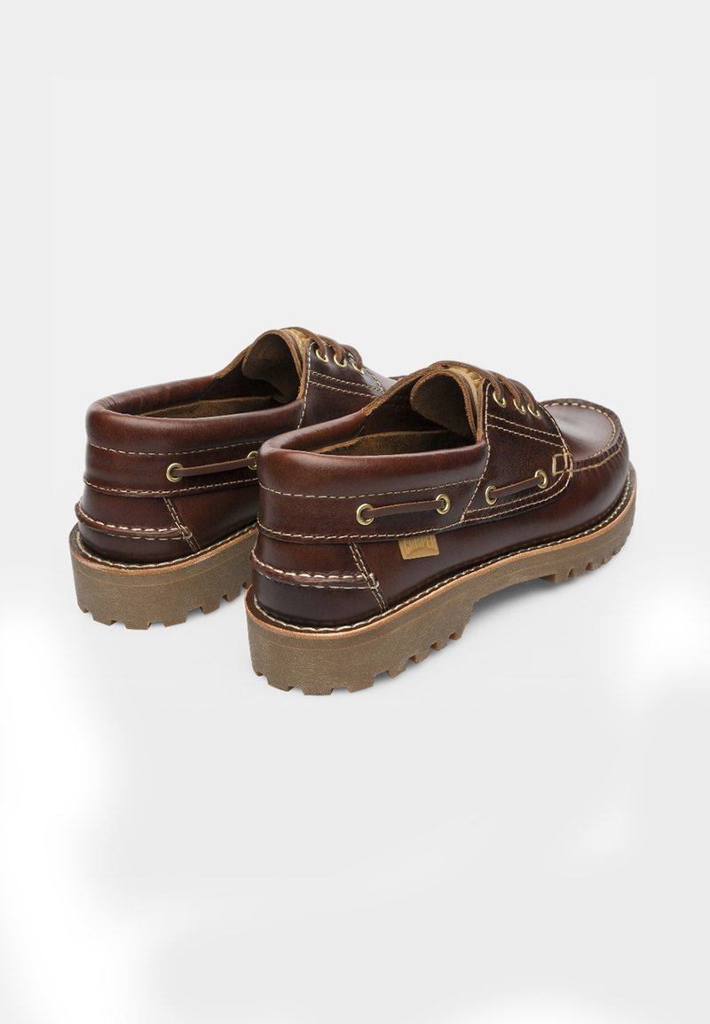 Une paire de chaussures bateau en cuir marron foncé avec des coutures beiges, des lacets ronds et des semelles en caoutchouc épaisses sur un fond blanc.