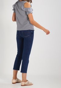 Czarna i biała bluzka w kratę gingham z wycięciami na ramionach, falbaniaste rękawy, zestawiona z ciemnoniebieskimi, krótkimi dżinsami oraz jasnobrązowymi plecionymi sandałami.