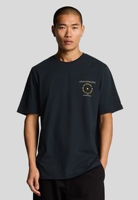 Svart bomull T-skjorte med korte ermer, med en frontgrafikk i gul tekst og sirkulært design. Klassisk passform med en glatt tekstur.