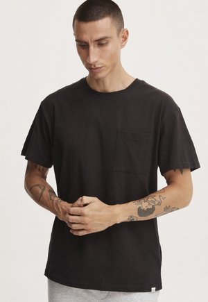 Camiseta de algodón negra con mangas cortas, cuello redondo y bolsillo en el pecho. Presenta un ajuste relajado y un detalle de dobladillo sin acabar.