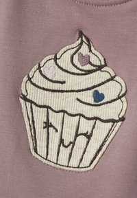 Gesticktes Cupcake-Design auf einem mauvefarbenen Pullover, das cremiges Frosting mit lila und blauen Herzakzenten sowie detaillierte gerippte Textur zeigt.