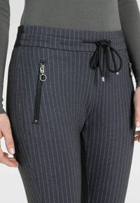 Dunkelblaue gestreifte Jogginghosen aus weichem Stoff mit einem Kordelzugbund, zwei Reißverschlusstaschen an den Seiten und kontrastierenden grünen Streifen.