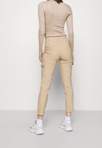 Beige cargo kalhoty s bočními kapsami, štíhlý střih, zkrácená délka, spárované s bílými teniskami a fitted béžovým žebrovaným dlouhým rukávem.