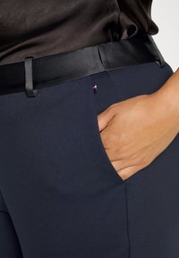 Marineblaue Hose mit schmalem Satinbund, seitlicher Tasche und einem kleinen Tricolor-Logo. Glatter Stoff mit taillierter Passform.