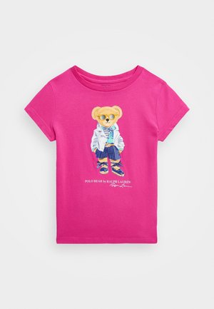 Kirkkaan pinkki lasten T-paita, jossa karhu aurinkolaseissa, valkoisessa takissa, raidallisissa shortseissa ja sandaaleissa. Tekstinä "Polo Bear by Ralph Lauren".