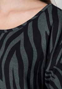 Langärmliger Pullover mit weitem Ausschnitt, der in einem grün-schwarzen Zebra-Streifen-Muster gestaltet ist. Hergestellt aus weichem, strukturiertem Strickmaterial.