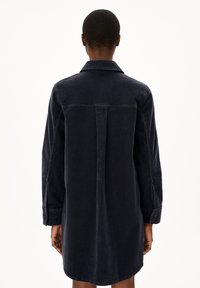 Dunkelblaues Cordhemdkleid mit langen Ärmeln, Knopfmanschetten, einer Rücknaht und einem geraden Schnitt, der bis zur Mitte des Oberschenkels reicht.