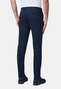 Granatowe spodnie wykonane z gładkiego materiału, z dwoma tylnymi kieszeniami z zapięciem na guziki oraz wąskim krojem. W zestawie z pasującymi ciemnymi butami.