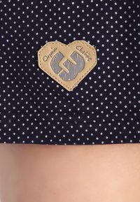 Granatowa tkanina w białe kropki, z oznaczeniem w kształcie serca z wytłoczonym napisem "Odzież organiczna" i logo.