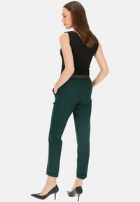Ciemnozielone dopasowane spodnie o gładkiej fakturze, z mankietami i bocznymi kieszeniami, zestawione z dopasowaną czarną bluzką bez rękawów.