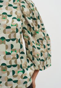 Bluză cu model în verde deschis, cu forme geometrice în nuanțe de verde și bej; are mâneci bufante și un tiv rotunjit.