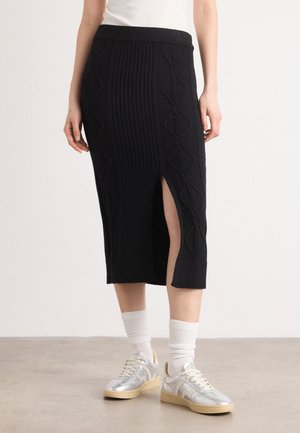 Zwarte gebreide midi-jurk met verticale ribbels en een zijsplit; gecombineerd met zilveren sneakers en witte crew-sokken.