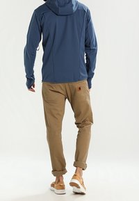 Blå hættejakke, beige bukser med opbøjedeÆrmer, beige sko. Bukserne er afslappede og har lommer, mens jakken har en glat overflade og syninger.