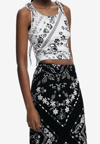 Mustat ja valkoiset leikattu tank-top, jossa on kukka- ja paisley-kuvioita, ohuet hihnat ja nyörisivut, yhdistettynä yhteensopivaan hameeseen.