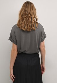 Top ampio e corto a maniche corte in tessuto grigio scuro, abbinato a una gonna nera plissettata con vita elasticizzata.