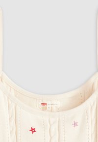 Camiseta de punto crema sin mangas con patrón de trenza; presenta estrellas bordadas decorativas en rojo y rosa. La etiqueta muestra la marca "Levi's", talla "S."