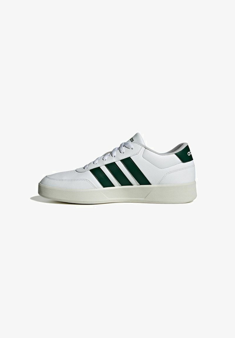 Zapatilla deportiva blanca con textura lisa de cuero, que presenta tres franjas verdes, puntera redonda y suela acolchada.