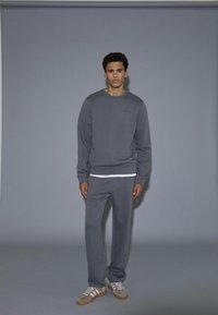 Grå sweatshirt och matchande mjukisbyxor i mjukt material, med en enkel design. Sneakers i grå, vit och beige ton kompletterar outfiten.
