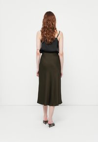 Top noir sans manches associé à une jupe olive mi-longue. La jupe a une texture lisse et s'éflare légèrement au niveau de l'ourlet.
