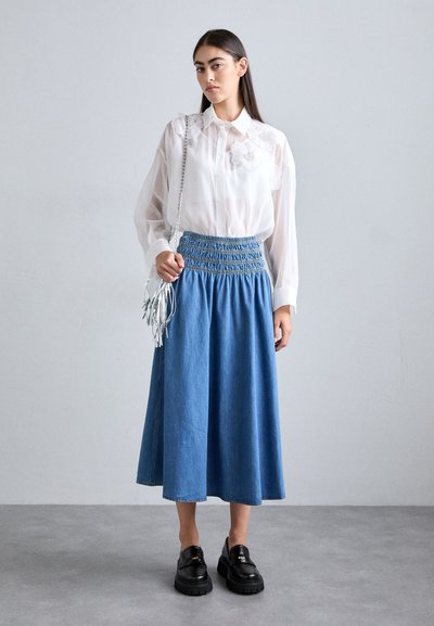 Hvid gennemsigtig bluse med blomsterapplikationer, parret med en blå denim midi-nederdel med smocket talje. Båret med kraftige sorte sko og en sølv taske.