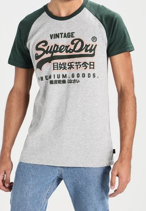 T-shirt gris à manches courtes avec des manches raglan vert foncé. Présente le texte "Vintage SuperDry" et un logo, avec une coupe décontractée.