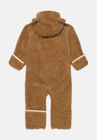 Une combinaison en polaire marron avec une capuche, présentant un tissu doux et texturé, ainsi que des rayures blanches sur les poignets et les jambes.