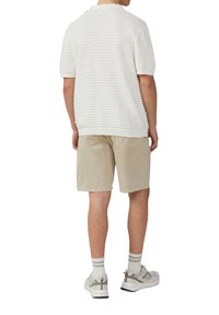 Witte gemêleerde polo met korte mouwen, gecombineerd met beige shorts. Het model draagt grijze sneakers met witte en grijze gestreepte sokken.