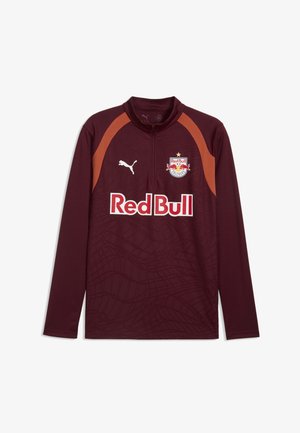 Bordowa sportowa koszulka z długim rękawem z pomarańczowymi akcentami na ramionach, logo Red Bull Salzburg, logo Puma oraz napis sponsora Red Bull w białym i czerwonym kolorze.