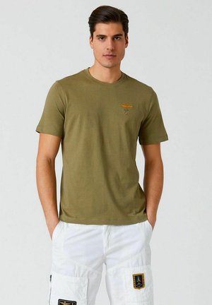 T-shirt in cotone verde oliva con collo tondo, maniche corte e un piccolo design ricamato arancione sul petto.