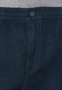 Navy blue textured shorts made from a waffle knit material, featuring an elastic waistband with a front button and side pockets.