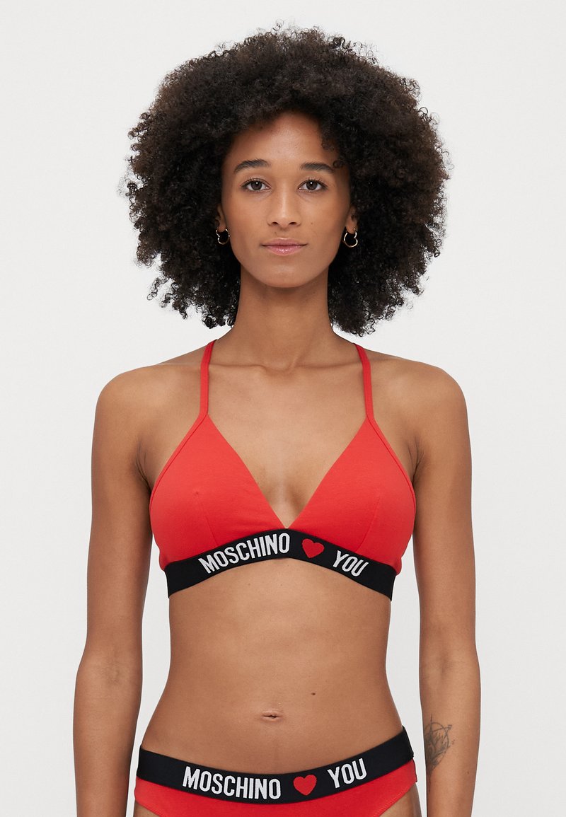Braletă roșie în formă de triunghi din material moale, cu bretele ajustabile și o bandă elastică neagră pe care este inscripționat "MOSCHINO ❤️ YOU" în text alb.