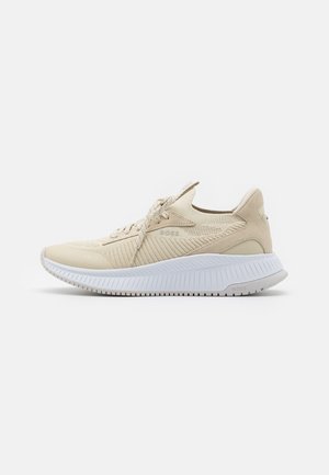 Beiger niedriger Schnürsneaker mit strukturiertem Strickobermaterial, gepolsterter weißer Sohle und markanten Details an der Seite und Ferse.