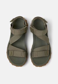 Vihreät kumisaappaat, joissa on ristirautadesign, teksturoidut pohjat ja säädettävät hihnat. Hihnoissa on logokoristeita.