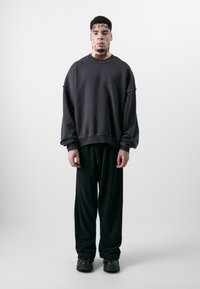 Felpa oversize grigia scura con maniche arrotolate, abbinata a pantaloni neri larghi e scarpe nere chunky. Colori solidi, dettagli minimi.