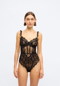 Črn čipkast bodi z motivom pik, podložene košarice, prosojne panele in cvetlične poudarke. Ima nastavljive naramnice in zapleteno detajliranje.