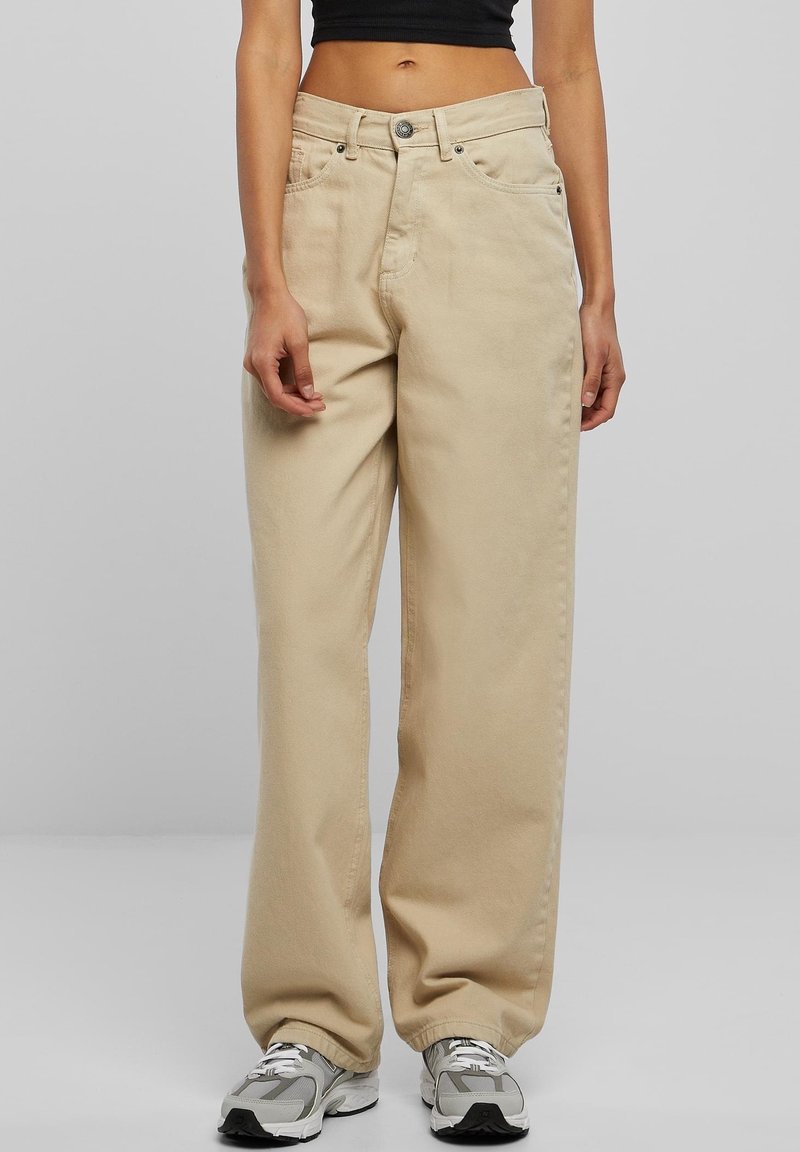 Krémové široké kalhoty s vysokým pasem, zapínáním na knoflík a předními kapsami; texturovaná denimová tkanina. Nosené se stříbrnými a šedými teniskami.