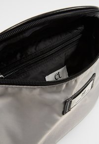 Szary satynowy worek zapinany na zamek błyskawiczny, wewnątrz z czarną podszewką, jedną kieszonką na zamek i metką z napisem "et". Miękka faktura o minimalistycznym wzornictwie.