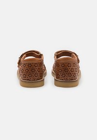 Brune lærsandaler med perforert design, justerbar spenne og gummisåle, med en glatt finish og rund form.