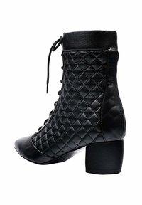 Botines negros con un patrón acolchado, puntera redondeada y tacón cuadrado. Presentan un cierre de cordones en la parte delantera y detalles de cuero liso.